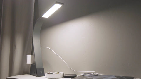 Image of a LUX Brooklyn AC LED Task Lamp in Black Slate on a contemporary minimalist desk next to a wallet and bowl with keys in it. There is a laptop power supply plugged into the Universal AC sockets on the back of the light.