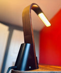 Brooklyn LED Task lamp in Black Walnut Wood finish on a wooden surface with a red background
