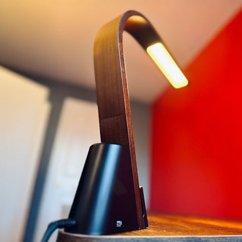 Brooklyn LED Task lamp in Black Walnut Wood finish on a wooden surface with a red background