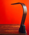 Brooklyn LED Task lamp in Black Walnut Wood finish on a wooden surface with a red background
