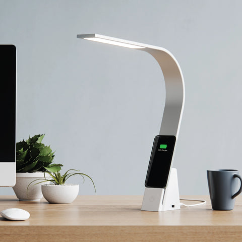 Brooklyn Aura LED Task lamp in Brushed Aluminum finish on a modern desk between two plants and a coffee cup. The USB-C port is visible, while the USB-A port is on the other side.