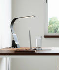 Brooklyn USB LED Task Lamp in Black Slate finish on a modern work desk with a phone charging via USB cord.