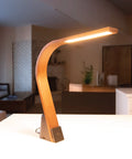 Flat paneled LED Task Lamp made out of Black Walnut wood sitting on a table in a midcentury modern living room. The light features 3000K dimmable light and USB ports.