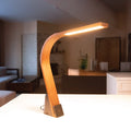Flat paneled LED Task Lamp made out of Black Walnut wood sitting on a table in a midcentury modern living room. The light features 3000K dimmable light and USB ports.