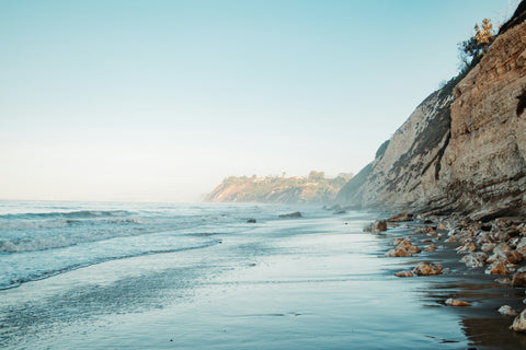 Daytime picture of a Santa Barbara beach with rugged cliffs hugging the sand and ocean. The tide is dropping and it's a beautiful morning. 