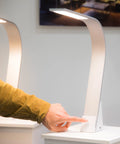Hand using the touch-sensitive brightness control on the Brooklyn USB LED Task Light in Brushed Aluminum with visible USB-A port.
