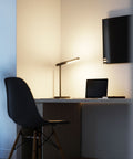 Highline USB LED Desk Lamp in use on a desk with a laptop and TV screen, showing warm upward and downward illumination