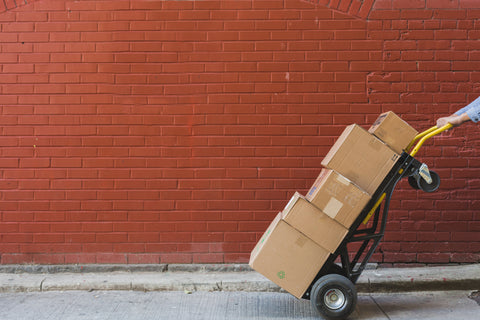 A delivery person pushing a dolly with five cardboard boxes on it, showcasing the speed and reliability of LUX shipments.