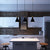 Three charcoal La Brea LED pendant lights hanging over a high top counter in a brick kitchen with white cabinets