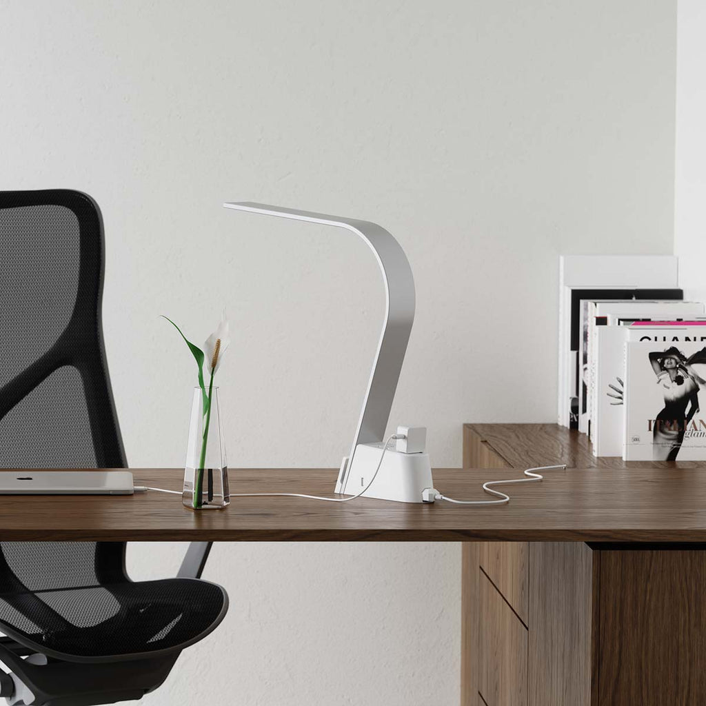 The Brooklyn AC LED Task Lamp on a desk with a computer plugged into one of the two Universal AC sockets integrated into the lamp's base.