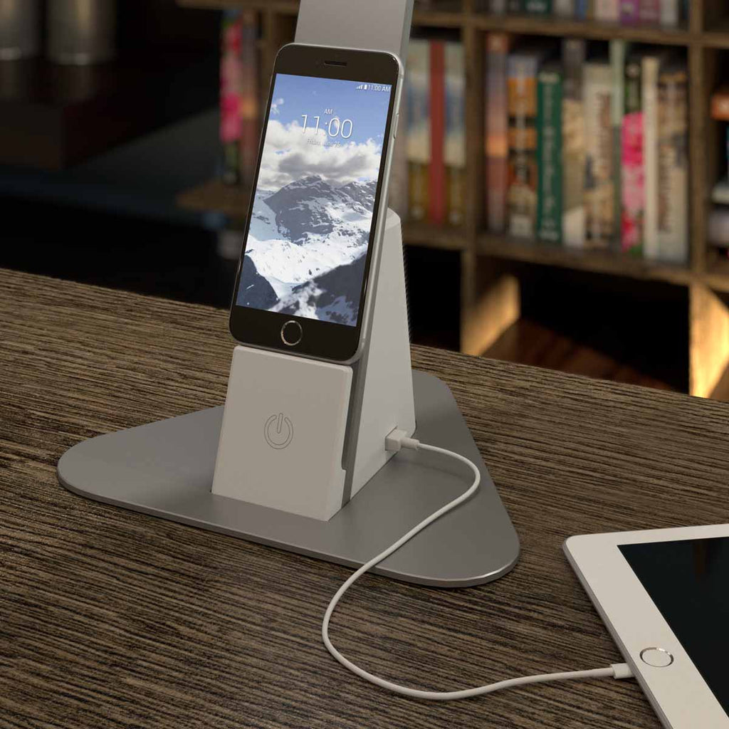 A smartphone is docked on the shelf of a Brooklyn LED Desk Lamp, which is charging also charging a tablet with a USB-C port